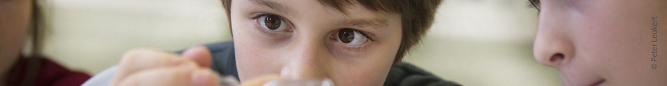 The picture shows a boy who is concentrating on an experiment object. In the background you can see other children who are also actively experimenting, which emphasizes curiosity and interest in learning.