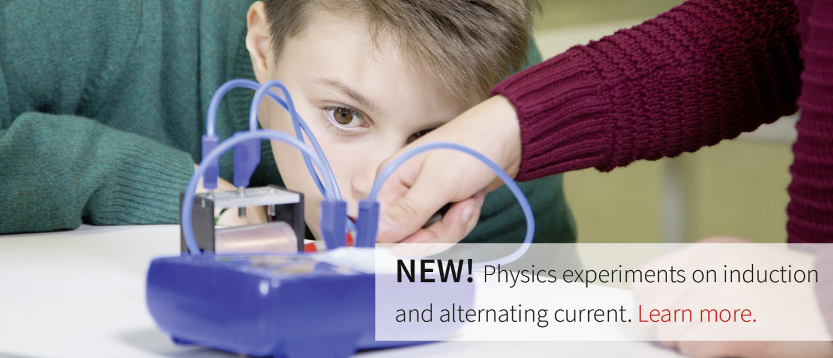 The picture shows a boy working concentratedly on a physics experiment device that has to do with induction and alternating current. One hand helps him experiment while colorful cables are connected to the device.