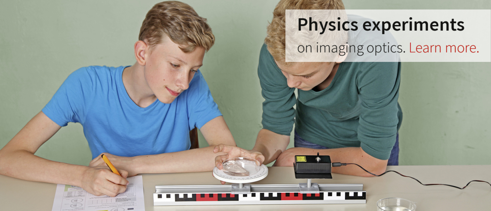 The picture shows two young people working intently on an experiment on image optics. They are using an optical lens and a measuring device while taking notes and analyzing the results.