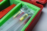 The picture shows a red storage box lined with green foam. Inside the box are transparent tubes with colored markings, probably used for experimental purposes in the educational field.