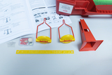The picture shows an experiment set for the topic &quot;Scales and balance&quot;. It contains various materials such as two yellow scales, a red holder, a yellow scale and instructions for experiments in the educational field.