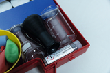 The picture shows a set of experimental supplies, which consists of various glass containers, a black measuring cylinder and a tube with a chemical substance. In addition, colored rubber cords are included in a yellow bowl, which can be used for experiments