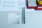 The picture shows a thermometer, a silver metal sheet and an open manual on a table. The materials are part of an experiment that deals with the conduction of heat and the reflection of light rays.