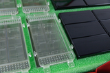 The picture shows several clear containers with compartments and some black rectangular plates on a green base. These materials are part of the experimental supplies designed for use in education.