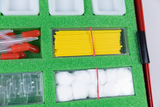 The picture shows a selection of experimental materials in a red box with green foam. Among other things, you can see pipettes with red caps, yellow sticks and cotton balls that can be used for various educational projects.