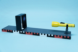 The picture shows an experimental device with a black box that projects a beam of light and a yellow flashlight mounted on a horizontal platform. The platform has a color-coded pattern that may be used to