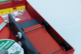 The picture shows an opened experiment box with various components, including round parts and a spool of string. The box is red and contains tools and materials used for practical experiments in education