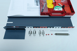 The picture shows various experimental materials, including an elongated metal plate, spring scales, weights and red clips. In addition, instructions and a plastic box with other accessories are visible, which are useful for experiments in the educational field. 