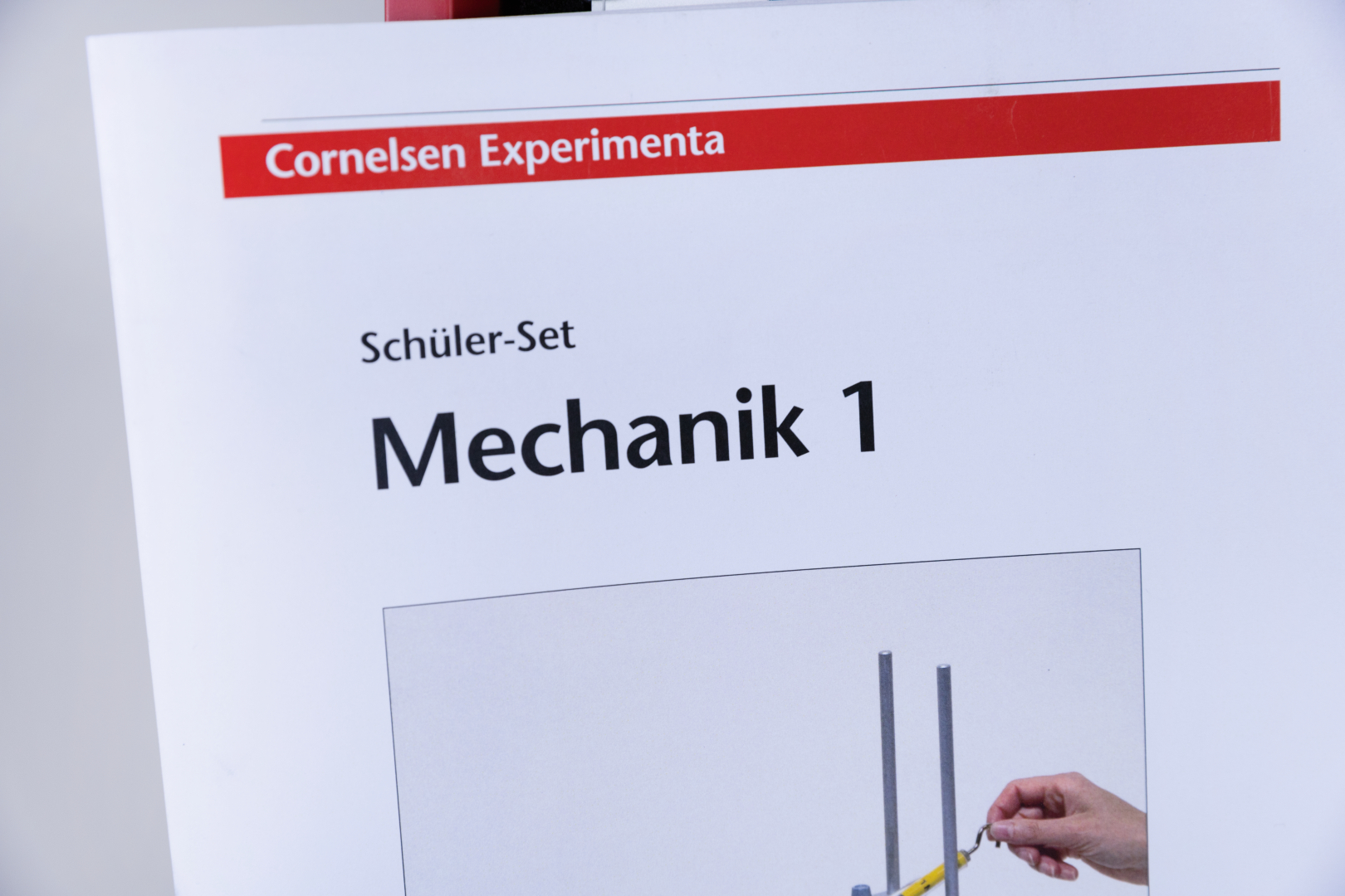 The picture shows the title of a student set with the theme &quot;Mechanics 1&quot; from Cornelsen Experimenta. Below is an illustration showing a hand handling an experiment set.