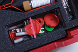 The picture shows a red plastic box filled with various experimental materials. Underneath are colored circles, tubes and other utensils, all arranged in a protective foam insert.