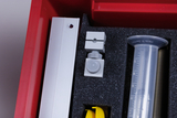 The picture shows a red storage box with various experimental materials. Inside there is a grey holder element, a measuring cylinder and other parts that can be used for scientific experiments in the educational sector