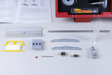 The picture shows a variety of experimental materials, including various mechanical components, a measuring cylinder and accessories stored in a red box. This also includes instructions, which are presumably intended for educational use.