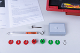 The picture shows a selection of experimental materials, including a spring force gauge, colored weight discs and a holder. In the background you can see instructions that provide questions and explanations for the experiments.