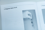 The image shows a hand holding a magnet while it is attached to two metal weights. The text next to it emphasizes that &quot;magnets have power,&quot; thus conveying the concept of magnetic attraction.
