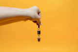 The image shows a hand holding an experimental device with two metallic weights attached to a red cable. The background is orange, which reinforces the focus on the experimental material and makes it attractive for educational purposes 