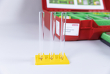 The picture shows three transparent test tubes standing on a yellow stand. In the background, a red suitcase with experimental materials for educational purposes is visible.