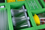 The picture shows a sorted toolbox with various experimental materials, including transparent test tubes, microscope slides and waterproof foils. The parts are safely arranged in a green foam pad to keep things organized and protected.