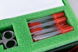 The picture shows the interior of a container lined with green foam. Inside are several pipettes with red caps and a small pair of scissors that can be used for experimental purposes in educational settings.