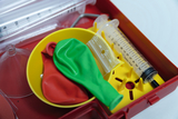 The picture shows an experiment box with various materials for teaching, including red and green balloons, a syringe and several transparent tubes. The items are arranged in a red box, which is suitable for practical experiments 