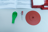 The picture shows a green latex bladder, valve and red platform that is part of an experiment kit. This set is used to demonstrate air pressure and movement in educational settings.
