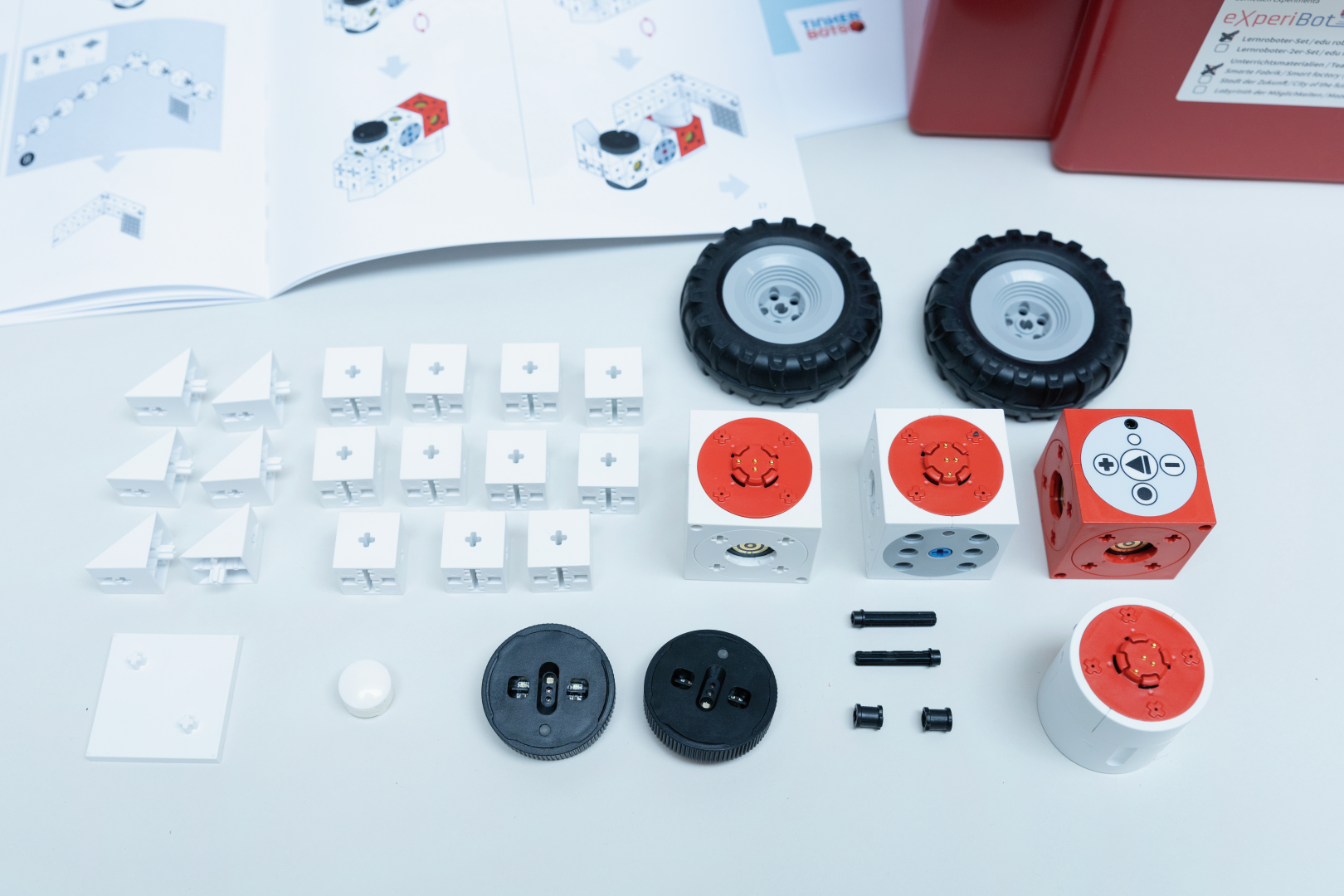 The picture shows a set of components for an educational toy that includes various modular cubes, wheels and connecting elements. Next to it is an instruction manual that explains how to assemble and use the components.