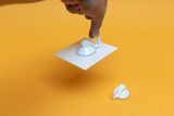 The image shows a hand holding a white experimental device with a suction cup, while another suction cup lies next to it. The background is a bright orange, which draws attention to the experimental material.
