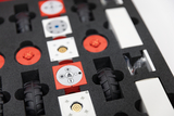 The picture shows an arrangement of various modular components in a foam insert that are used for experiential learning purposes. Red and white elements can be seen, including wheels and control boards, which create interactive projects.