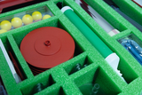 The image shows a selection of experimental materials neatly arranged in a green foam insert. Visible objects include red plates, yellow balls and a green cylinder, which are suitable for various scientific experiments.