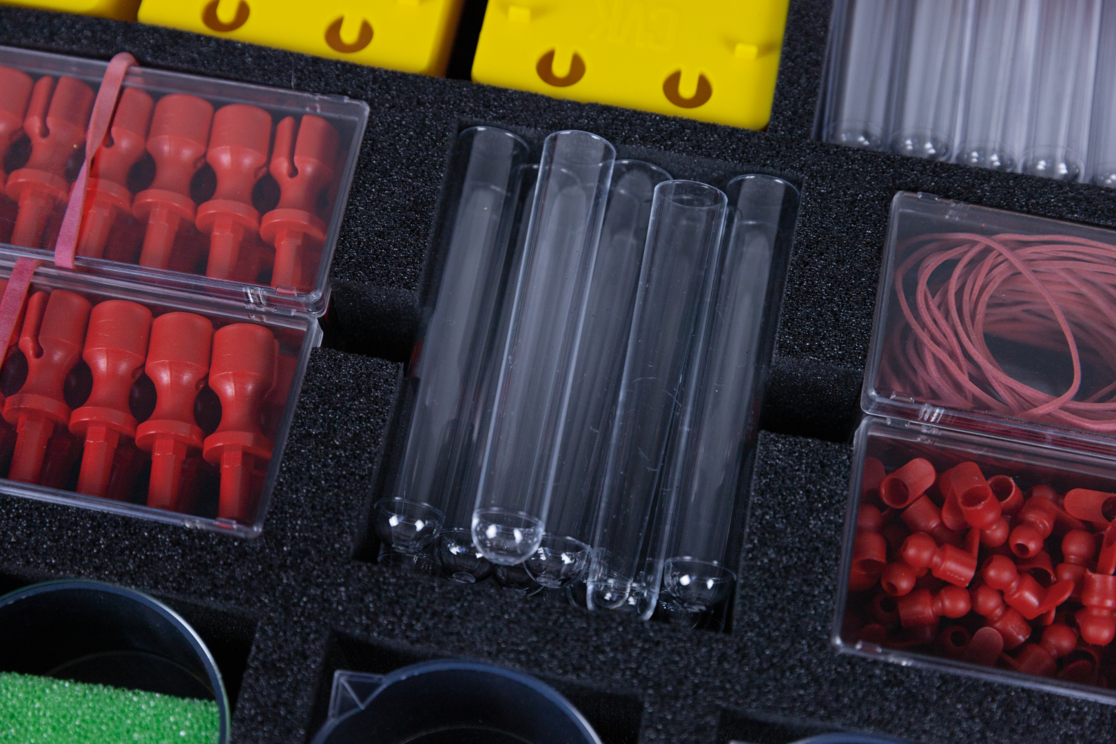 The picture shows a selection of experimental materials, including transparent test tubes and various red and yellow plastic parts in a padded box. The arrangement of the parts suggests use for teaching and research purposes in the bi