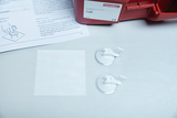 The picture shows an experiment kit with two suction cups, a transparent sheet and instructions. It is part of a teaching material that focuses on air pressure and related physics experiments.