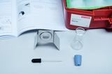 The picture shows an experiment kit with an instruction manual, a tripod, an Erlenmeyer flask, a pipette and a blue stopper. These materials are intended for educational experiments on heat.