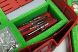 The picture shows a red storage box with green foam in which several transparent, red test tubes are stored. In addition, small compartments are visible in the upper part of the box, which contain various accessories.