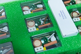 The picture shows a set of experimental materials organized in a green padded case. It contains various components such as light bulbs, screws and small objects for experimental purposes in educational settings.