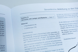 The picture shows instructions for experiments with a lamp and a battery from a textbook for the German education system. It lists the materials needed, including a flat battery and a light bulb, as well as important information on the D