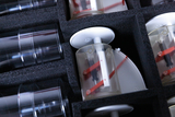 The picture shows an arrangement of experimental equipment, including several transparent cylinders and mechanical components in a padded box. The parts appear to be designed for experimental purposes in the educational field and are safely stored