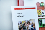 The picture shows a student set for experimenting with water, presented by Cornelsen Experimenta. In the foreground you can see children carrying out various experiments together, demonstrating curiosity and teamwork.