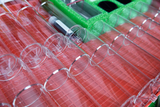 The picture shows an arrangement of transparent test tubes on a red holder, which are used for experimental purposes in the educational sector. In the upper area, other materials and accessories are also visible in a green insert.