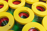 The picture shows a collection of transparent containers with yellow lids and red inserts. The containers are arranged symmetrically and stand on a green base, which gives a fresh, three-dimensional impression.