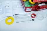 The picture shows an experiment set with various tools, including a transparent tube, a corresponding container and a spoon. There is also a manual that contains instructions for conducting experiments.