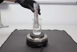 The image shows a scientist immersing a thermometer into a glass of water placed on a heating block. The heating block is ready to heat the water while the temperature is read from the thermometer.