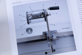 The image shows a mechanical device called a DynaMot, intended for experimental applications in education. It is housed in a clear case and focuses on showing various parts such as the motor