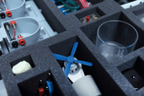 The picture shows a compact storage with various experimental materials, including a small blue propeller, electrical components and a glass container. These materials are neatly arranged in compartments to provide structured access 