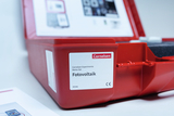 The picture shows a red storage box with the label &quot;Cornelsen Experimenta Photovoltaic Demo Set&quot;. In the background you can see an information page that probably offers further details about the contents and applications of the set.