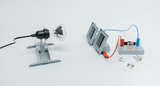 The picture shows an experimental equipment consisting of a lamp holder with a light bulb and an experimental board with electrical components. Next to it are various plugs that can be used for electrical connections.