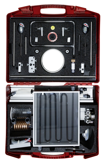 The picture shows an open red suitcase containing various scientific experiment tools and equipment. These include pipes, gauges, valves and a solar absorber, which are used for educational purposes in science classes