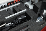 The picture shows a suitcase with various experimental equipment organized in foam-padded compartments. Among other things, you can see a cable, a lamp and metal parts that can be used for educational purposes.