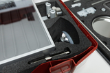 The picture shows a plastic box filled with foam padding and containing several experimental technical components. You can see a transparent lid, metal parts and other objects that are used for experiments in education.