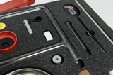 The picture shows a storage box with various experimental materials arranged on a foam-padded insert. Among the items are geometric shapes, glass tubes and other components that are used for scientific