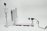 The picture shows an experimental setup with a lighting element on the right and a measuring device on the left, which is attached to a tripod. In the middle there is a horizontal base with colored markings that 