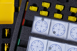 The picture shows a collection of experimental materials, including several compasses in protective cases and yellow plastic parts that may serve as stands or holders. Also visible are pens in green and red, which are used for technical drawings.